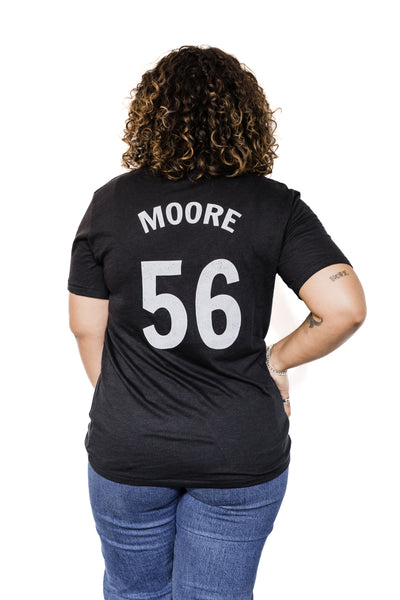 Back of Black female model wearing a Marianne Moore #56 black unisex baseball tee