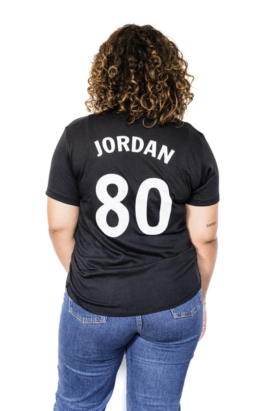Back of Black female model wearing a June Jordan #80 black unisex tee