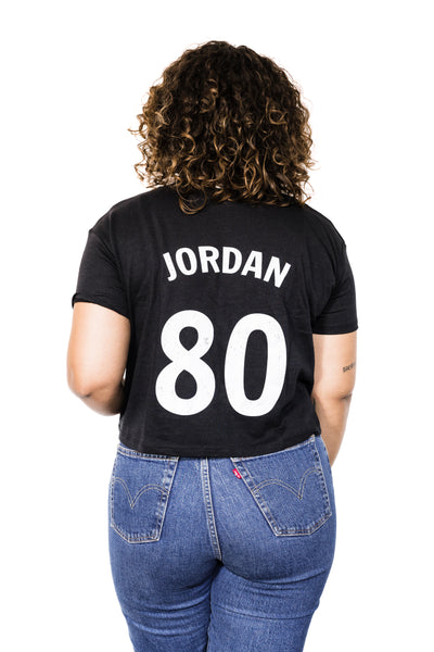 Back of Black female model wearing a June Jordan #80 black crop tee