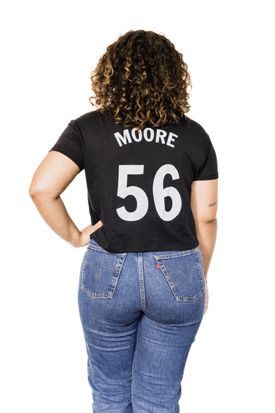 Back of Black female model wearing a Marianne Moore #56 black crop baseball tee